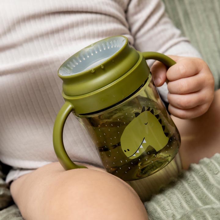 Baby holding a Trixie Tritan 360° cup with a fun animal design of Mr. Dino.